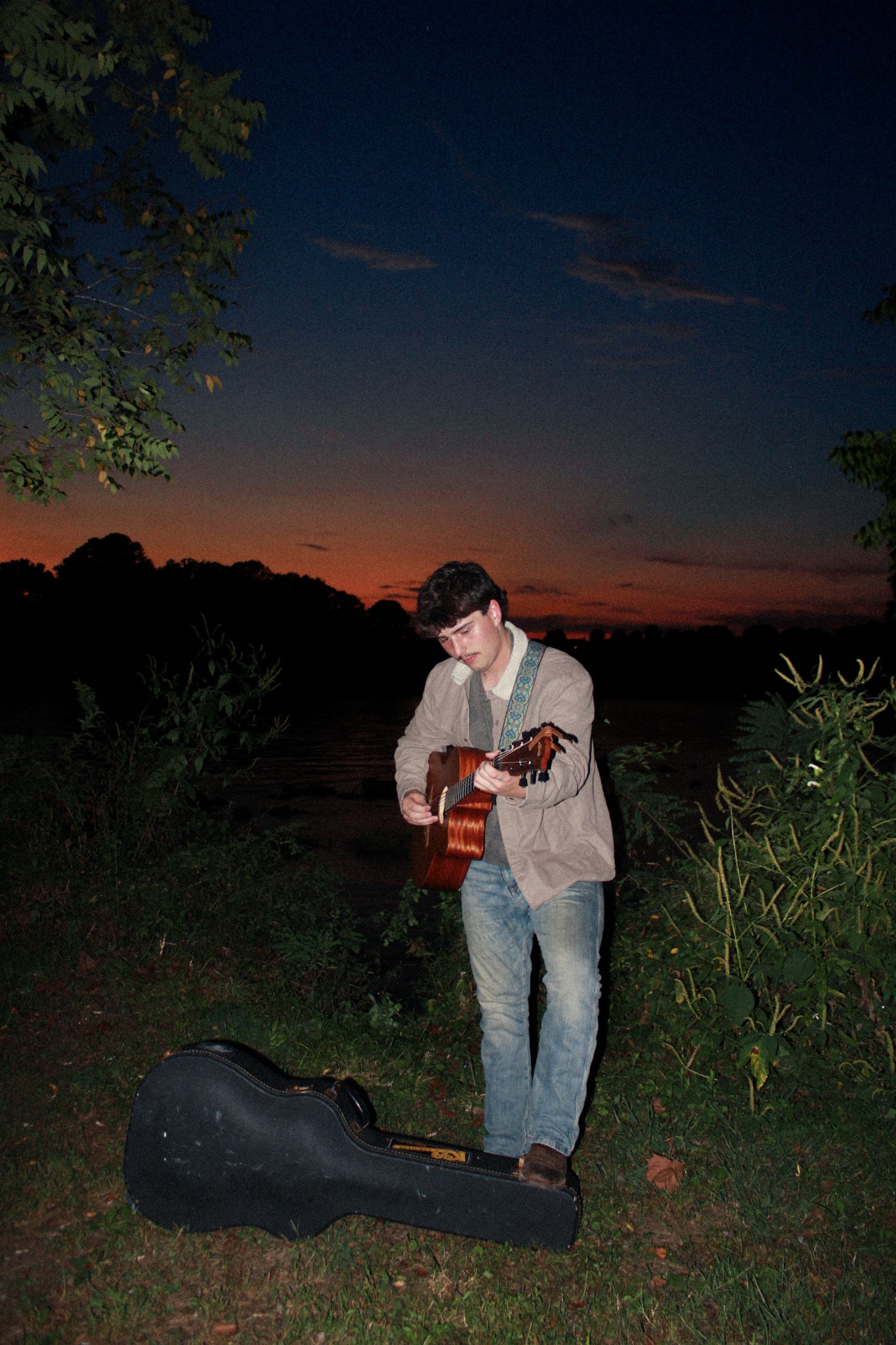 Torben Mucchetti playing guitar by the water at sunset
