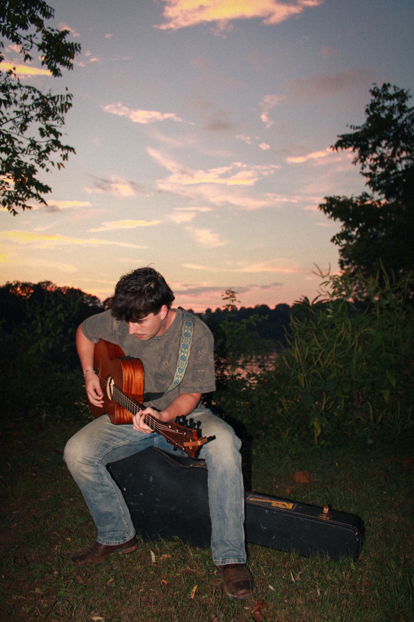 Torben Mucchetti sitting with guitar outdoors at sunset